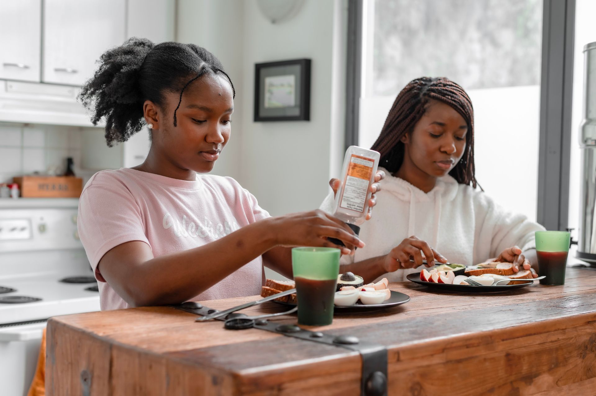 Two women having breakfast at a wooden kitchen table with drinks.