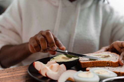 Free Close-up of hands preparing avocado toast with boiled eggs and apple slices, ideal for health-focused meals. Stock Photo