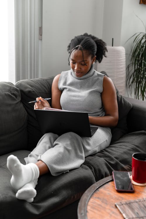 Woman in Gray Tank Top Sitting on Black Couch Using Laptop