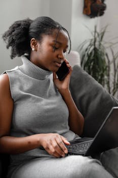 Young African American woman multitasking with a laptop and phone, exemplifying remote work lifestyle.