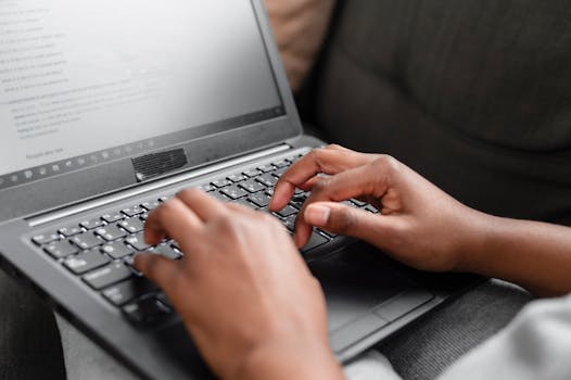 Close-up of hands typing on a laptop keyboard, working from home setting.