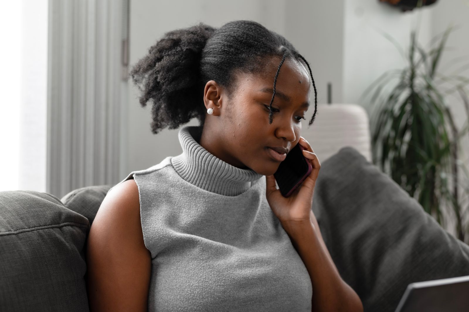 A Black woman sits on a couch with a phone to her ear, listening closely on a call. This is the call the guide tells you to make: to your health plan, the hospital patient advocate, or a clinic front desk.