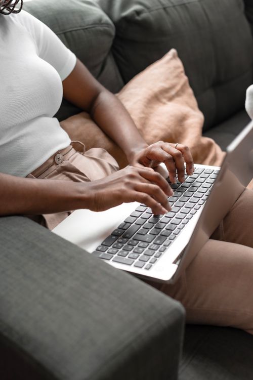 Free Woman sitting on sofa typing on laptop, comfortable home setting. Stock Photo