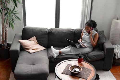 Woman Using a Laptop and Talking on the Phone While on a Sofa