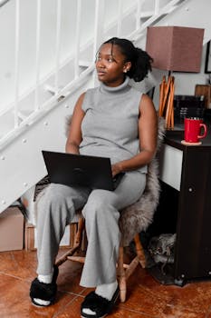 African American woman sitting with a laptop, working remotely indoors under a staircase.