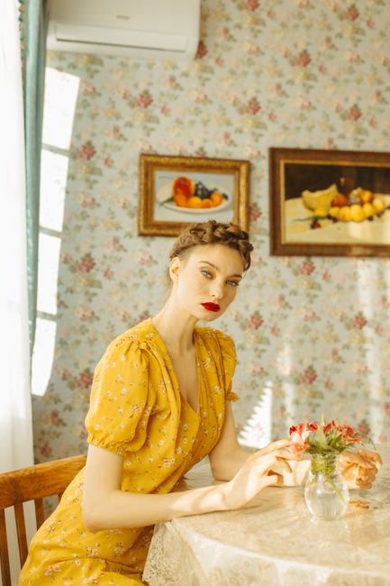 Elegant woman in vintage floral setting, sitting at table in yellow dress.