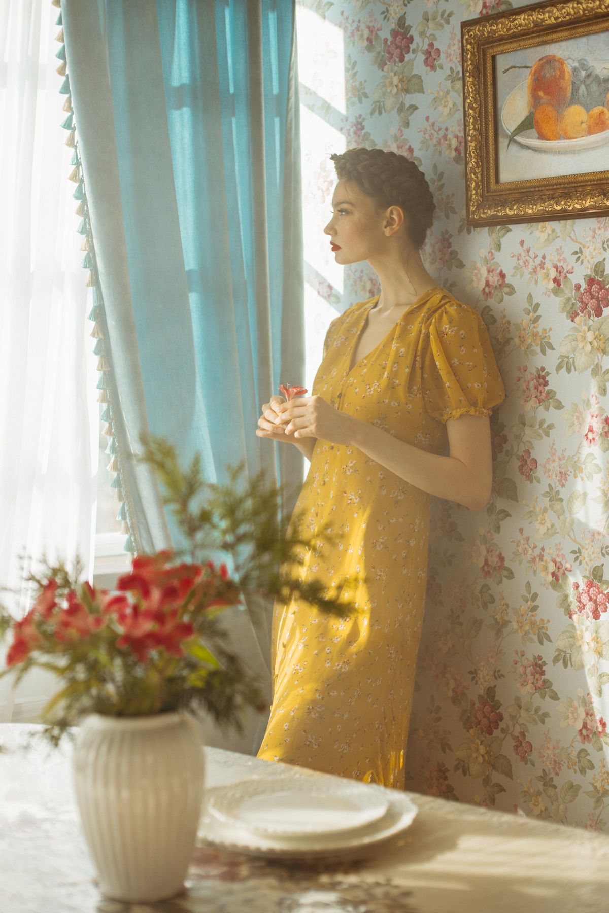 Woman in a mustard floral dress beside a sunlit window in a vintage interior
