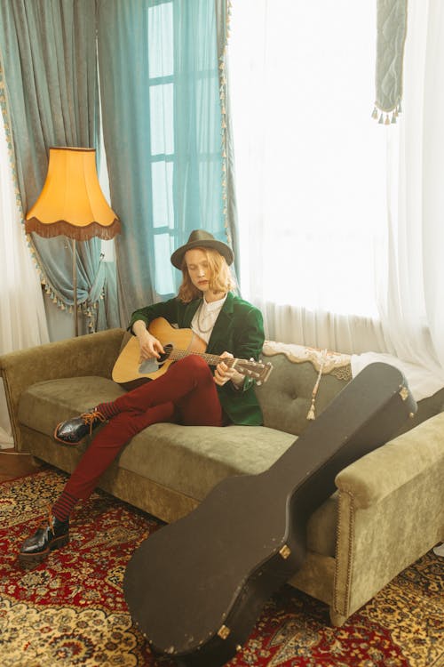 A Man Sitting on Sofa Playing the Guitar