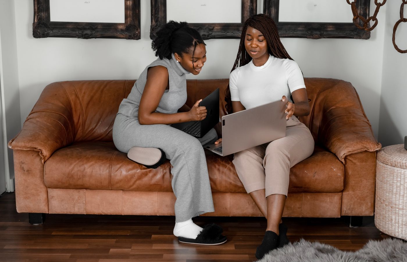 Two African American women working together on laptops in a cozy indoor setting.