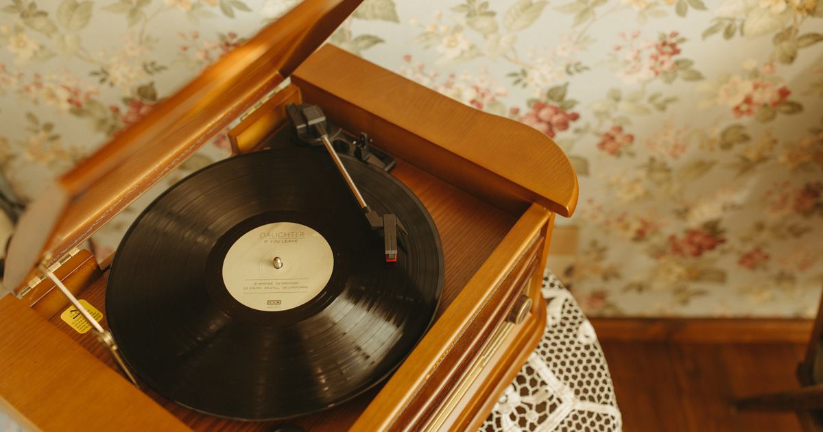 A vintage turntable playing a vinyl record in a cozy, retro interior with floral wallpaper.