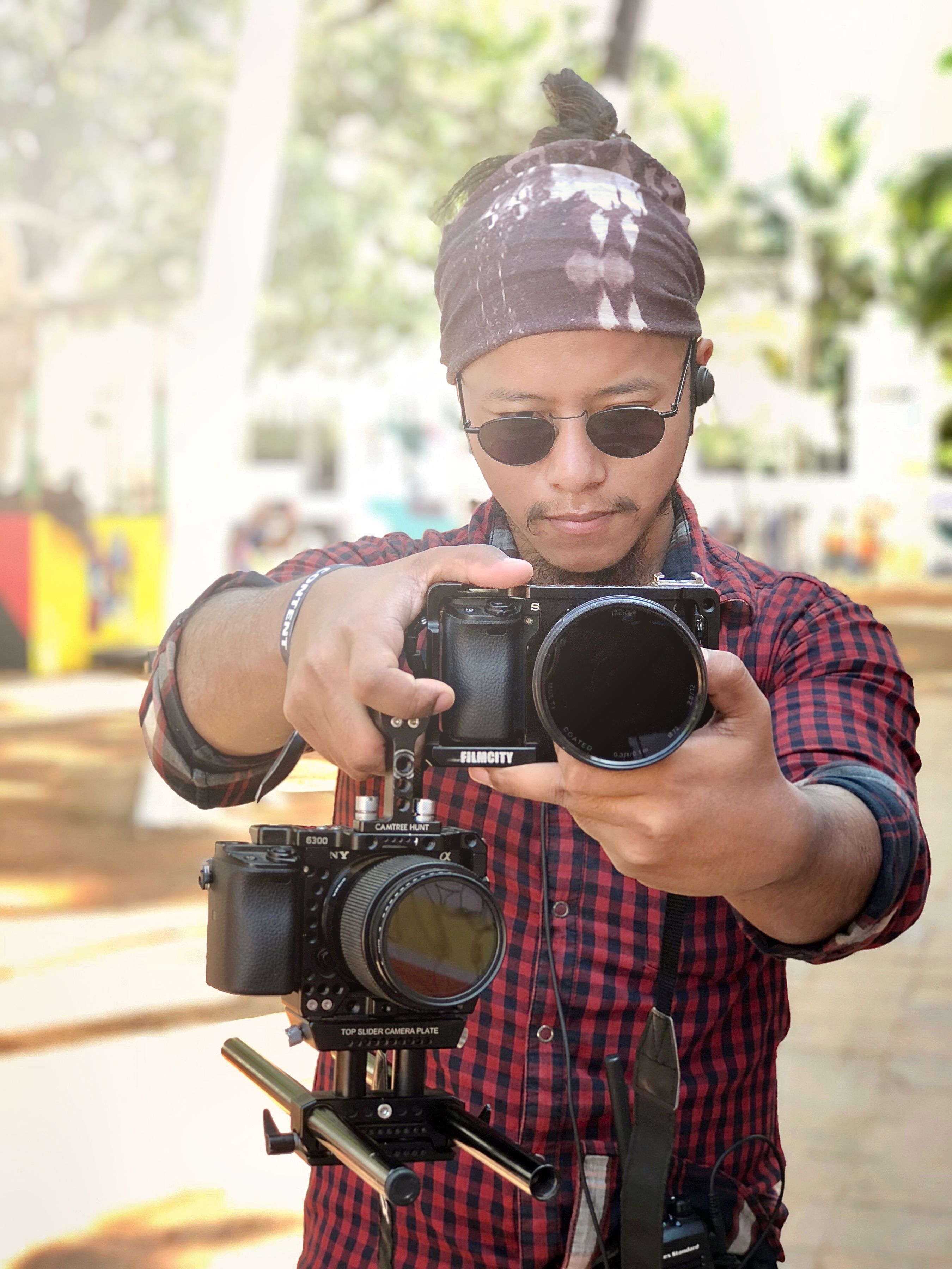 A focused videographer adjusting his camera setup in an outdoor setting, capturing high-quality footage.