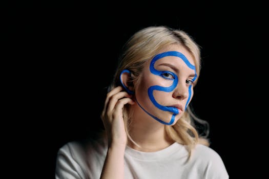 Artistic portrait of a woman with creative blue face makeup on a dark background.