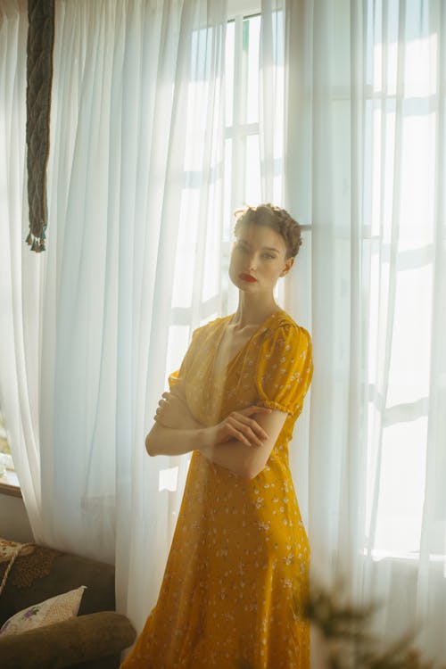 A Woman Wearing a Yellow Dress Standing by the Window · Free Stock Photo