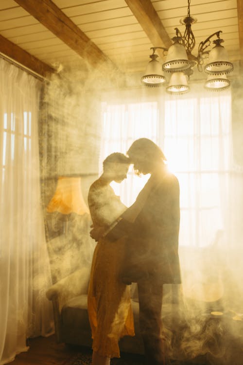 Free Couple Backlit by the Sun Flare Through the Window with Curtain Stock Photo