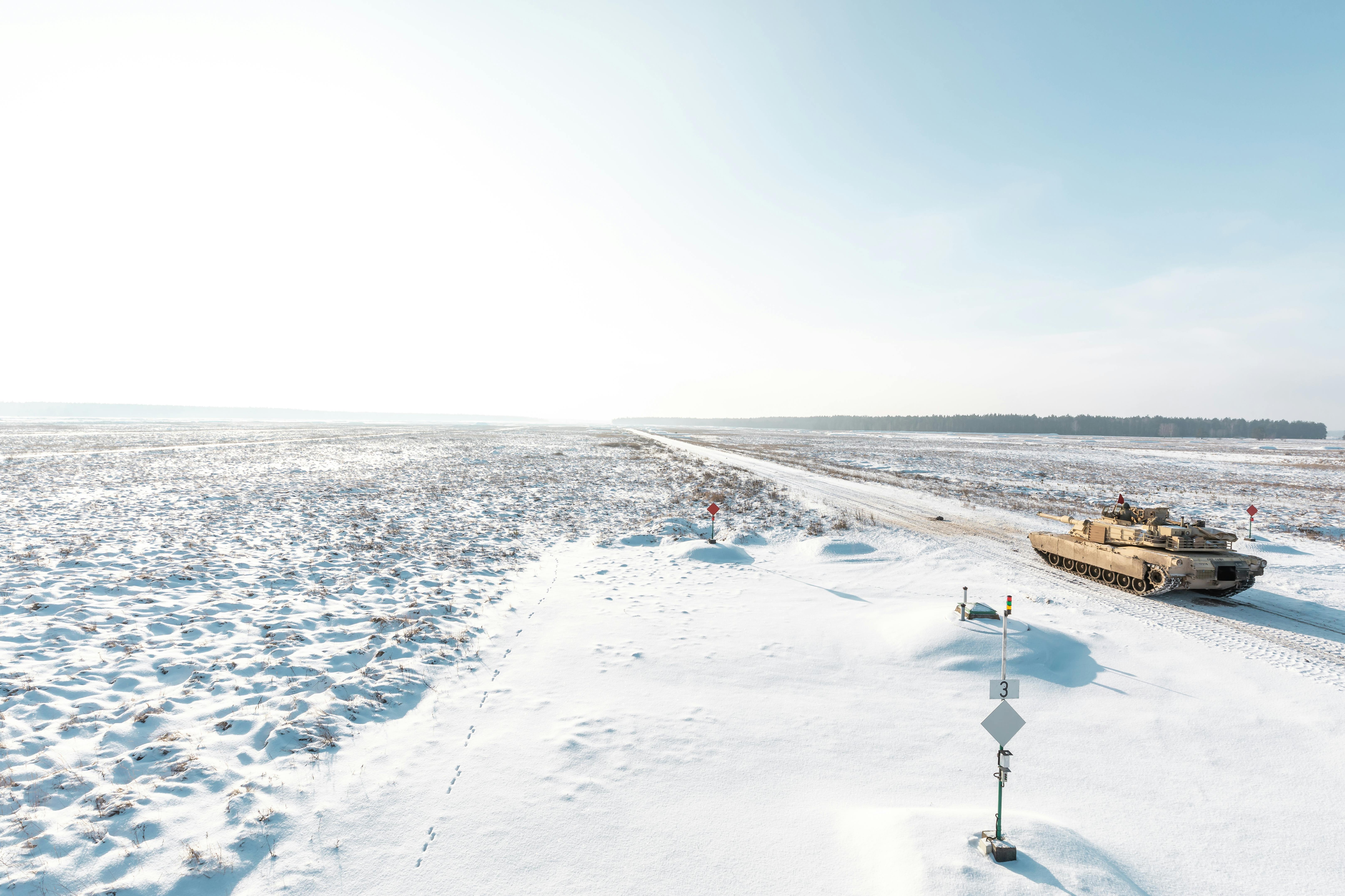 Military tank driving through a vast snow-covered terrain, conveying a scene of isolation and power.