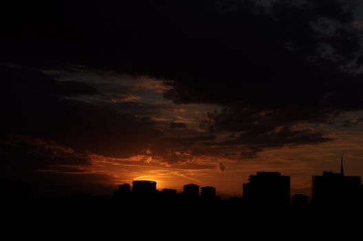 Silhouette of city buildings against a dramatic sunset sky with vibrant colors.