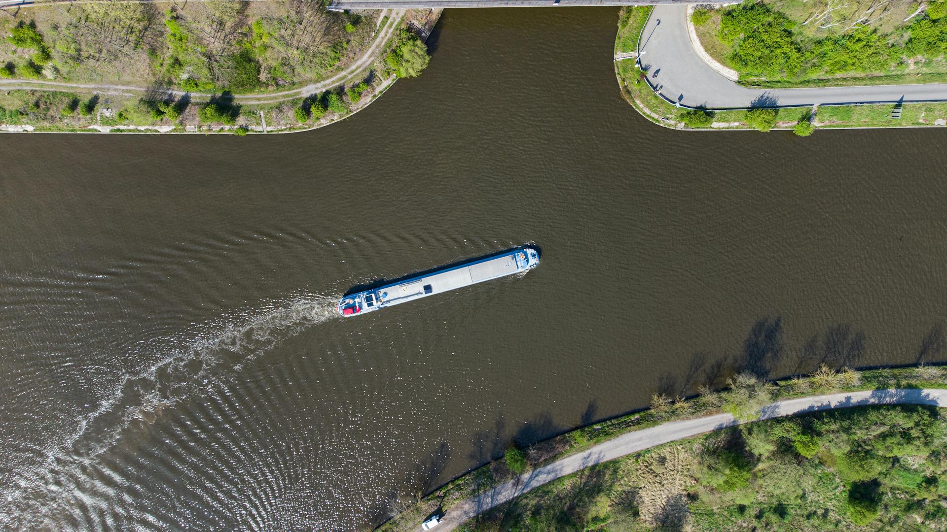 Aerial view of a ship sailing through a scenic canal surrounded by greenery, showcasing tranquil waterway travel.