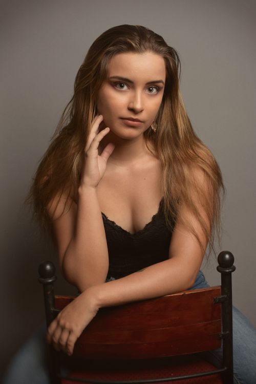 Free Portrait of a young woman posing on a chair in a studio environment, capturing elegance and grace. Stock Photo