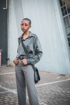 Fashionable woman wearing sunglasses and chic outfit posing in urban Johannesburg street.