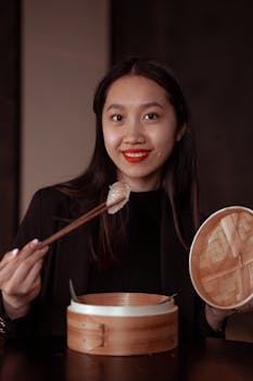 Smiling Asian woman holding dumplings with chopsticks, enjoying traditional cuisine.