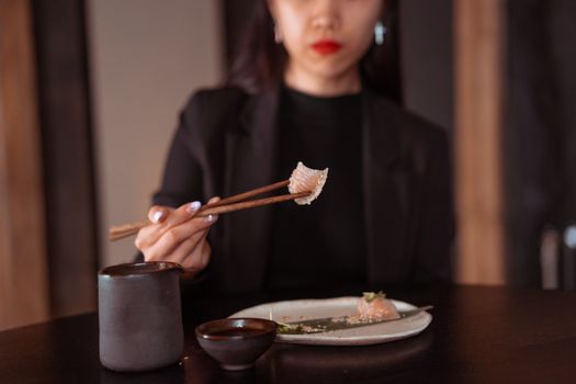 A woman in a black outfit uses chopsticks to pick up dim sum in a cozy dining setting.