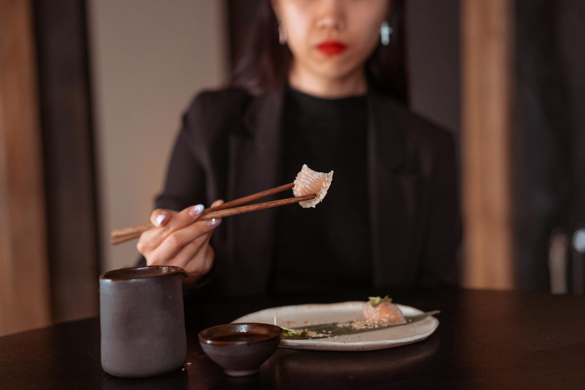 A woman in a black outfit uses chopsticks to pick up dim sum in a cozy dining setting.