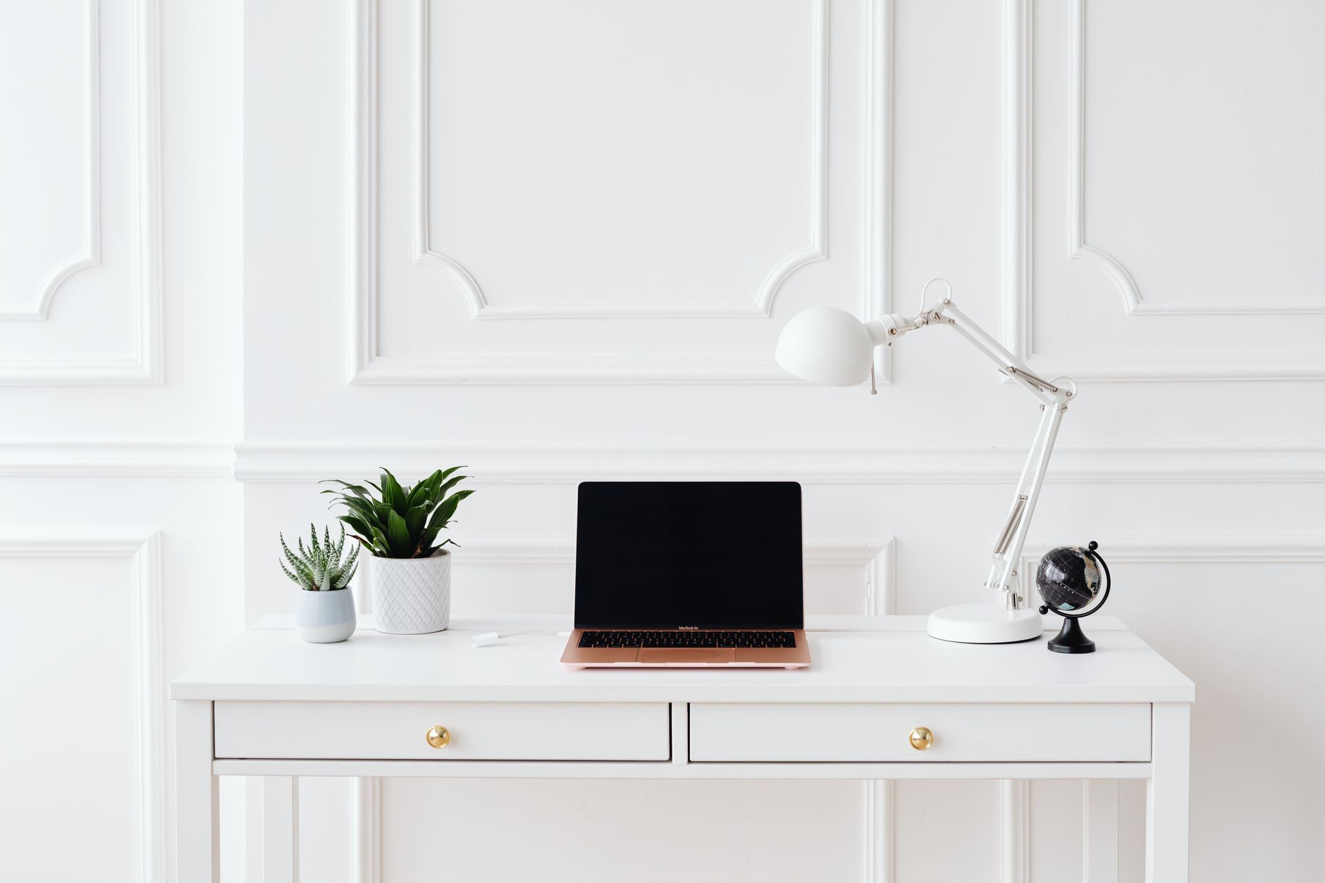 A minimalist home office setup featuring a laptop on a white desk with decor items.