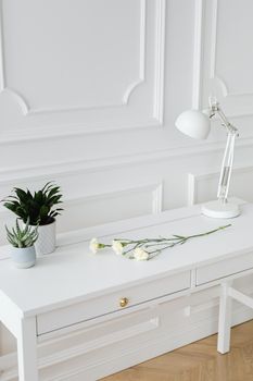 Elegant minimalist white desk setup with lamp, plants, and roses, perfect for a tranquil workspace.