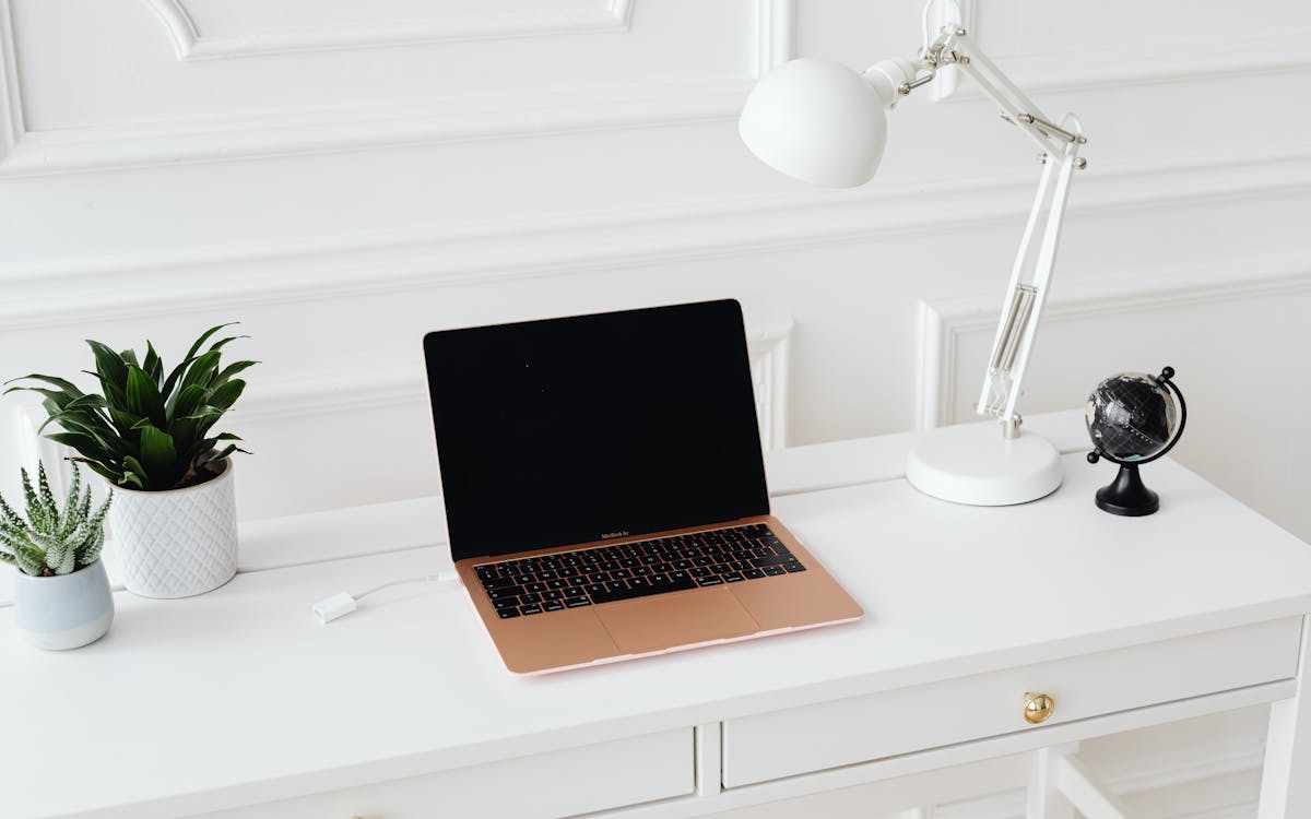 Clean and stylish workspace featuring a laptop, desk lamp, and potted plants on a white desk.