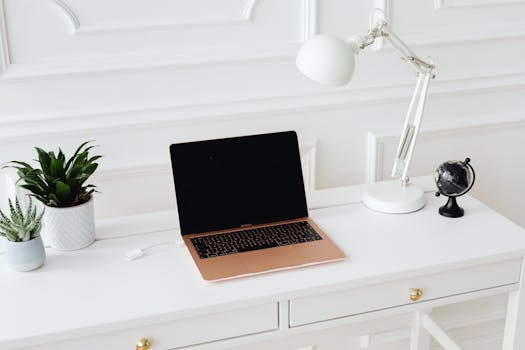 Clean and stylish workspace featuring a laptop, desk lamp, and potted plants on a white desk.