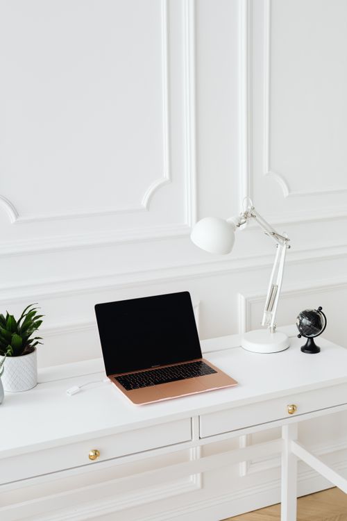 Free A tidy minimalist workspace featuring a laptop and desk lamp on a white desk. Stock Photo