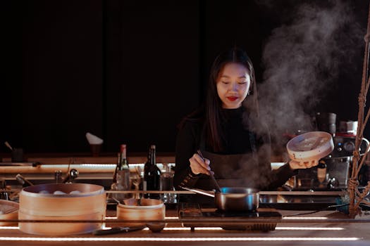 A woman prepares food with a steamer in a cozy kitchen setting, surrounded by culinary tools.
