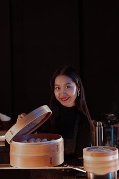 Smiling Asian woman holding a food steamer with dumplings.