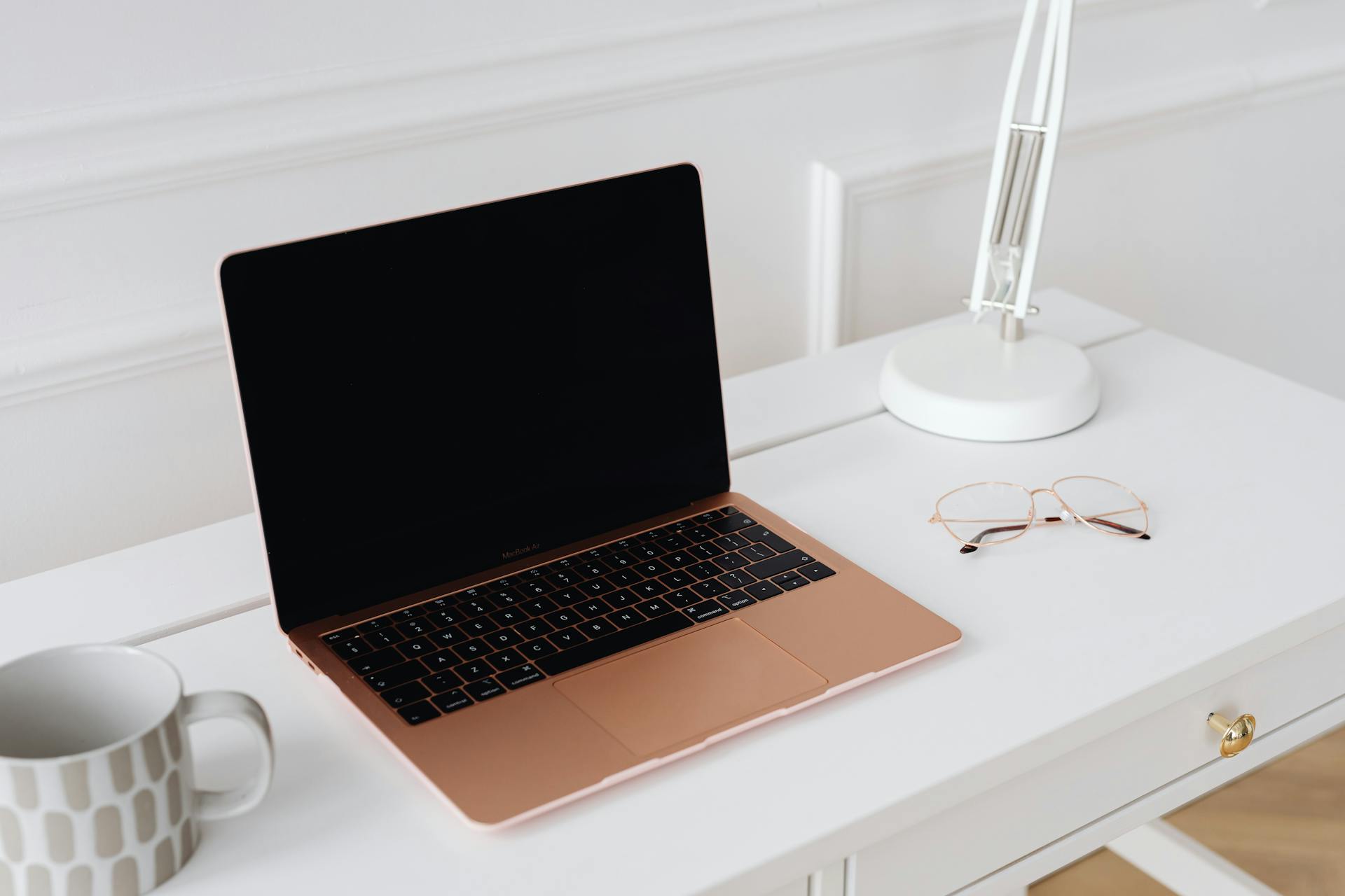 A modern sleek workspace featuring a laptop, desk lamp, and glasses on a white table.