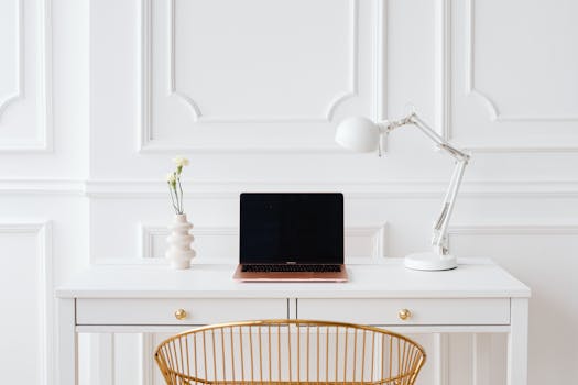 Elegant minimalist workspace with a laptop on a white desk, adorned with a modern lamp and decorative vase.