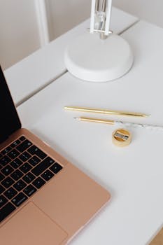 A tidy and minimalist workspace featuring a laptop, pen, pencil, and sharpener on a white table.