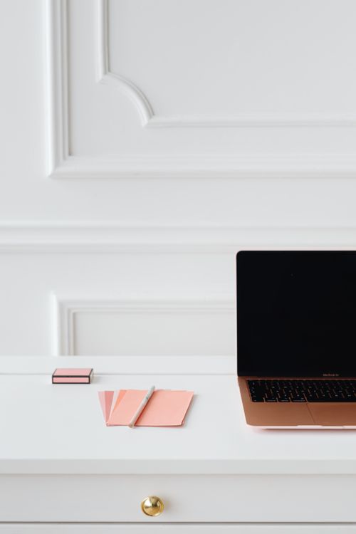 Free A minimalist workspace featuring a laptop, notepad, and pink stationery on a white desk. Stock Photo