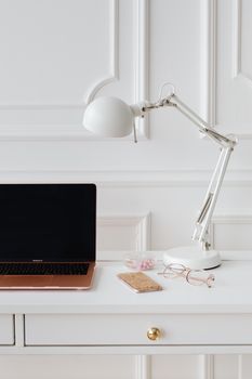 Elegant workspace featuring a laptop, eyeglasses, lamp, and phone on a minimalist desk.