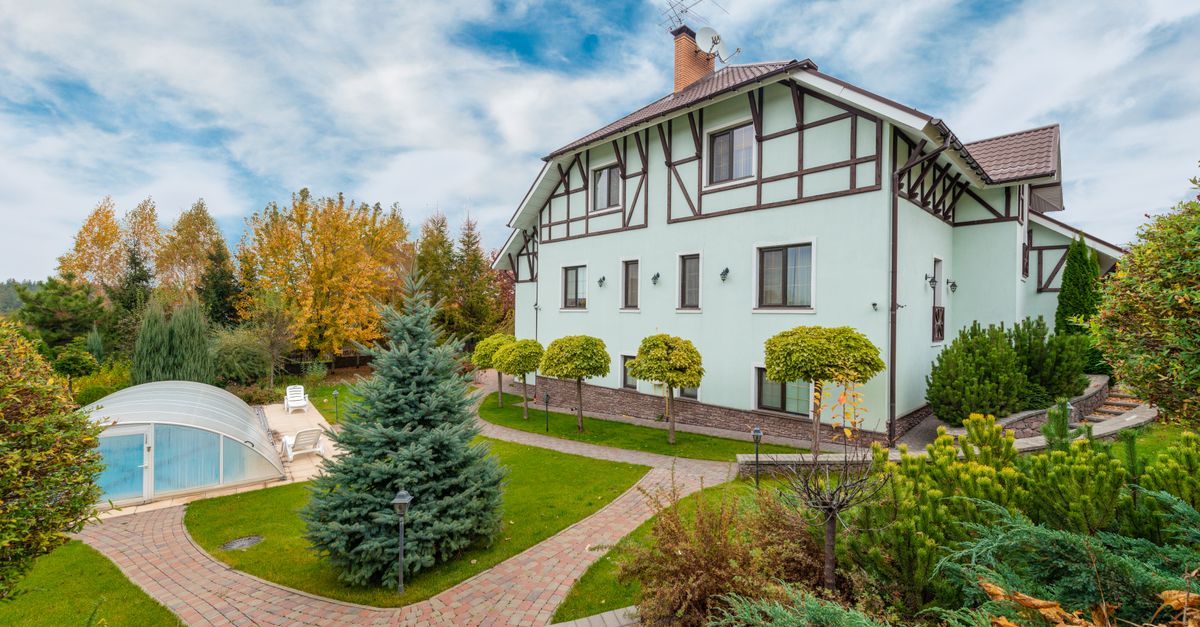 Tudor-style home with landscaped garden and pool under a vibrant cloudy sky.