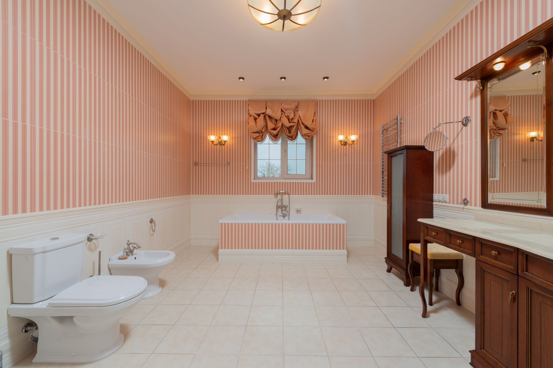 Spacious classic bathroom with vanity furniture, bathtub, wallpaper and warm finishes