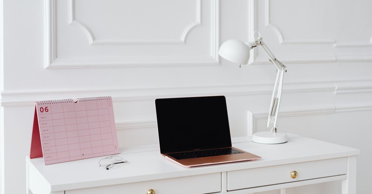 Simple desk setup with laptop, calendar, and lamp in a bright, minimalist office setting.