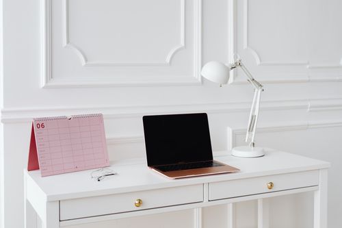 Free Simple desk setup with laptop, calendar, and lamp in a bright, minimalist office setting. Stock Photo