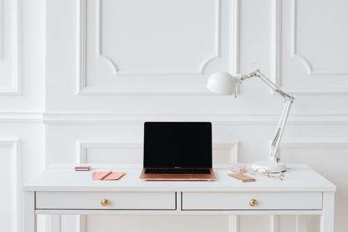 Free A clean and bright workspace with a laptop, desk lamp, and essentials on a white table. Stock Photo