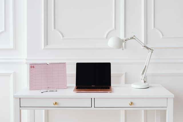 A laptop and desk calendar on a white table.