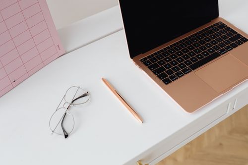 Free A clean and organized workspace with a laptop, planner, glasses, and pen on a desk. Stock Photo