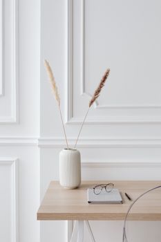 Stylish minimalist desk with ceramic vase, pampas grass, and eyeglasses creating a serene workspace.