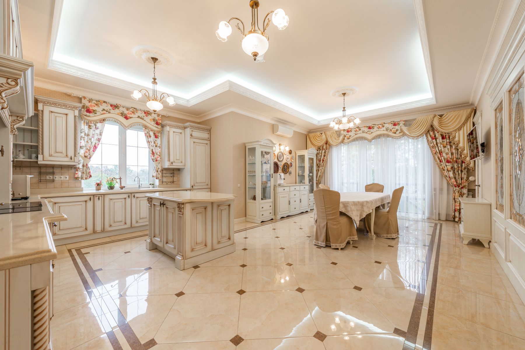 Cream kitchen and dining area with decorative pendant lights, floral curtains and upholstered chairs