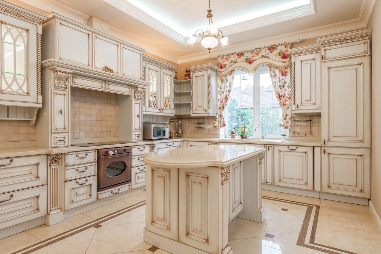 Ornate traditional cream kitchen with carved cabinets, a central island, and floral window curtains