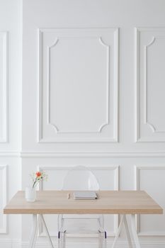 Elegant, minimalist desk with transparent chair and floral decor in a bright white room.