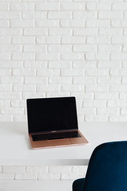 Free A sleek modern workspace featuring a laptop on a white table against a textured brick wall. Stock Photo